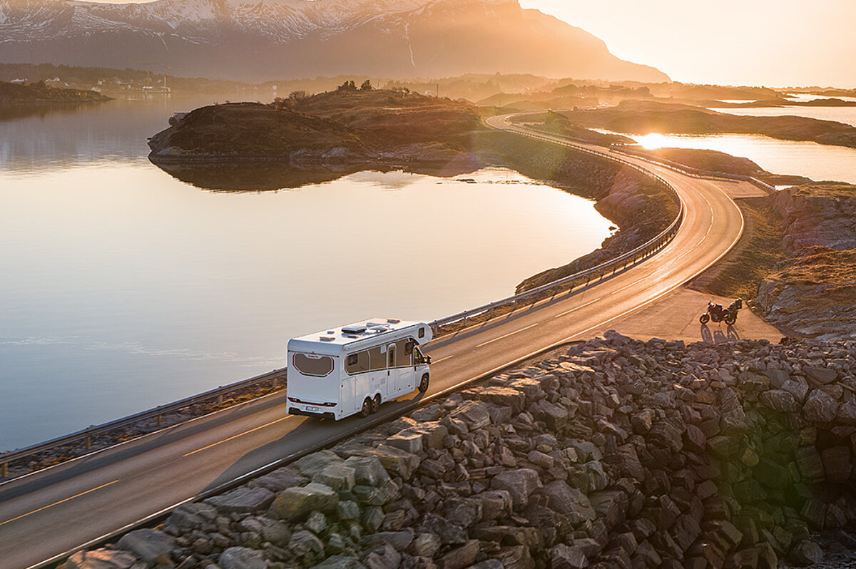 Ein Wohnmobil fährt eine Küstenstraße entlang in den Sonnenuntergang.