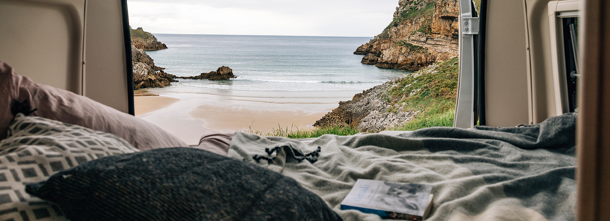 Blick aus dem Heck eines Camper Vans direkt auf einen Strand.