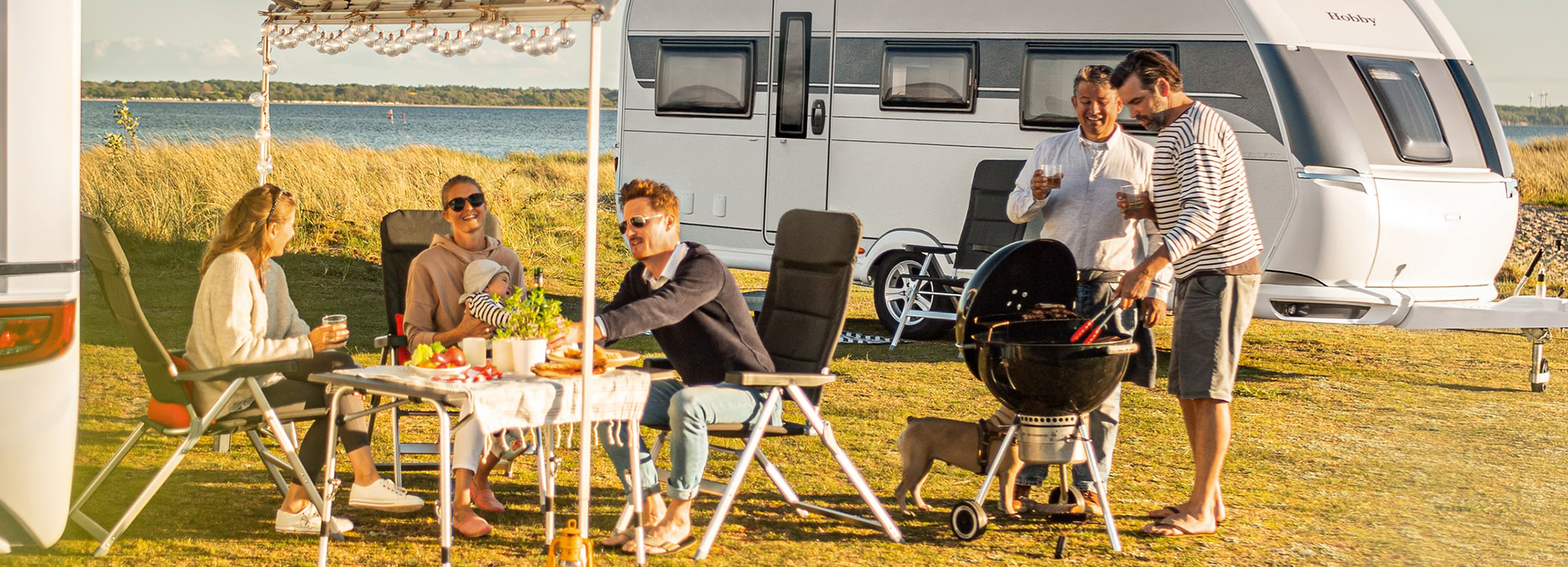 Zwei Familien grillen gemeinsam vor ihren Freizeitfahrzeugen.