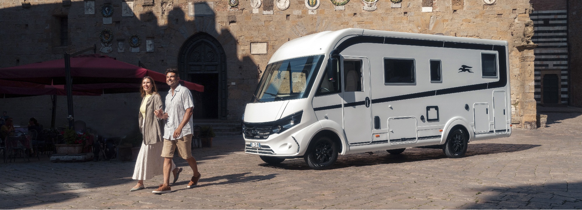 Ein Paar spaziert im Urlaub vor einem Wohnmobil, das sie über Inzahlungnahme finanziert haben.