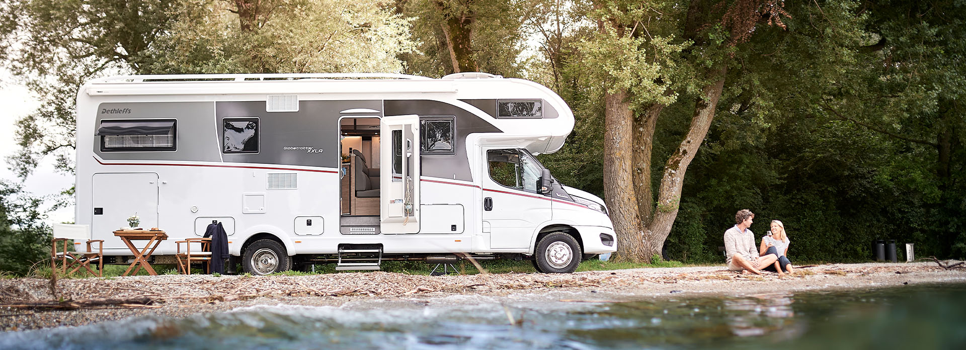 Ein Paar sitzt am See neben einem Wohnmobil.