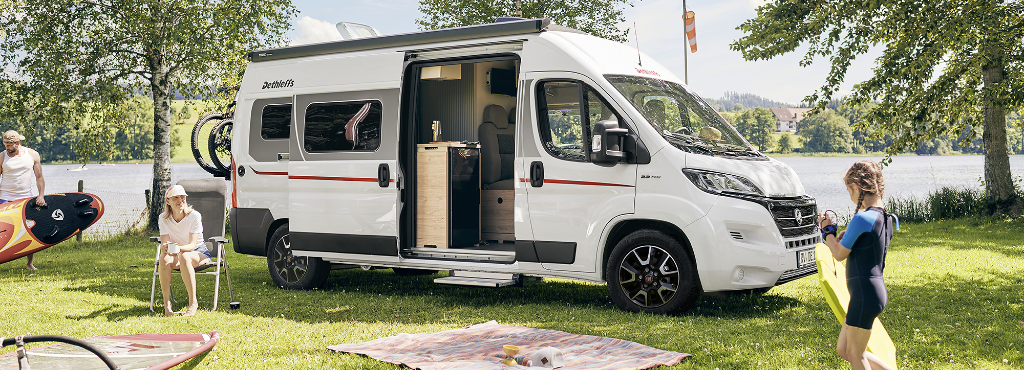 Eine Familie trägt Surfbretter neben einem Dethleffs Wohnmobil.