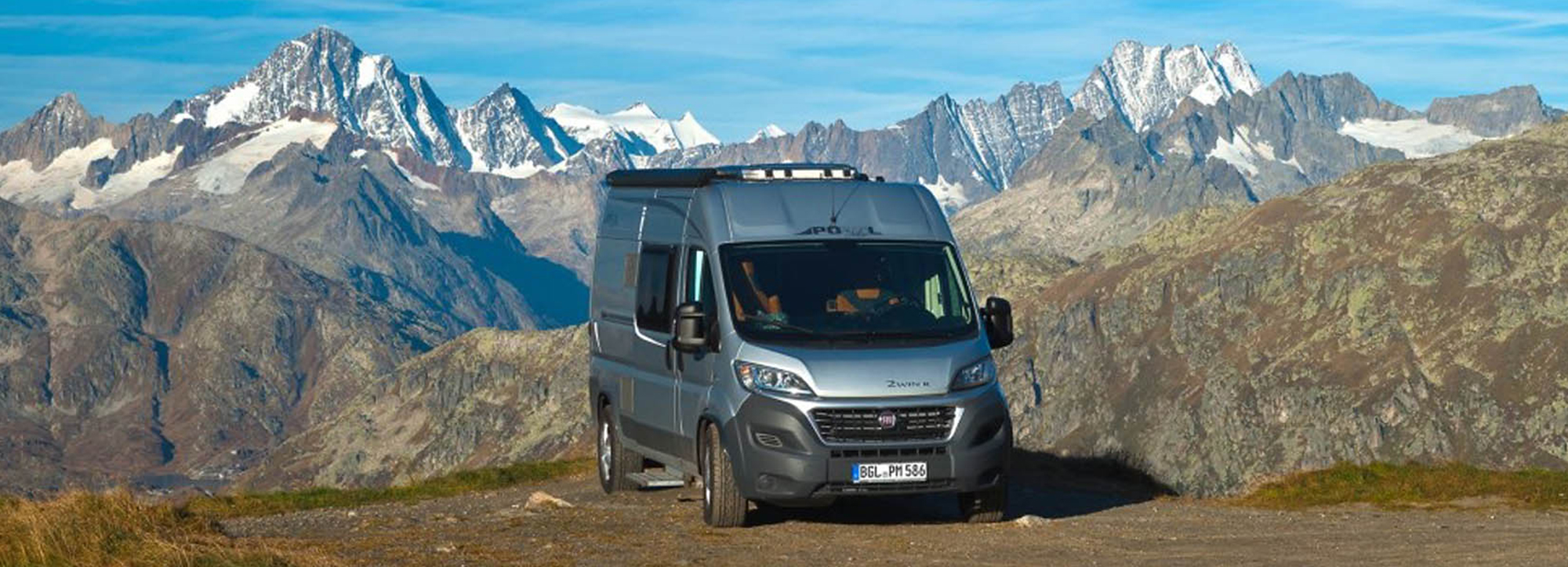 Ein Camper Van von Pössl fährt durch Berggelände.