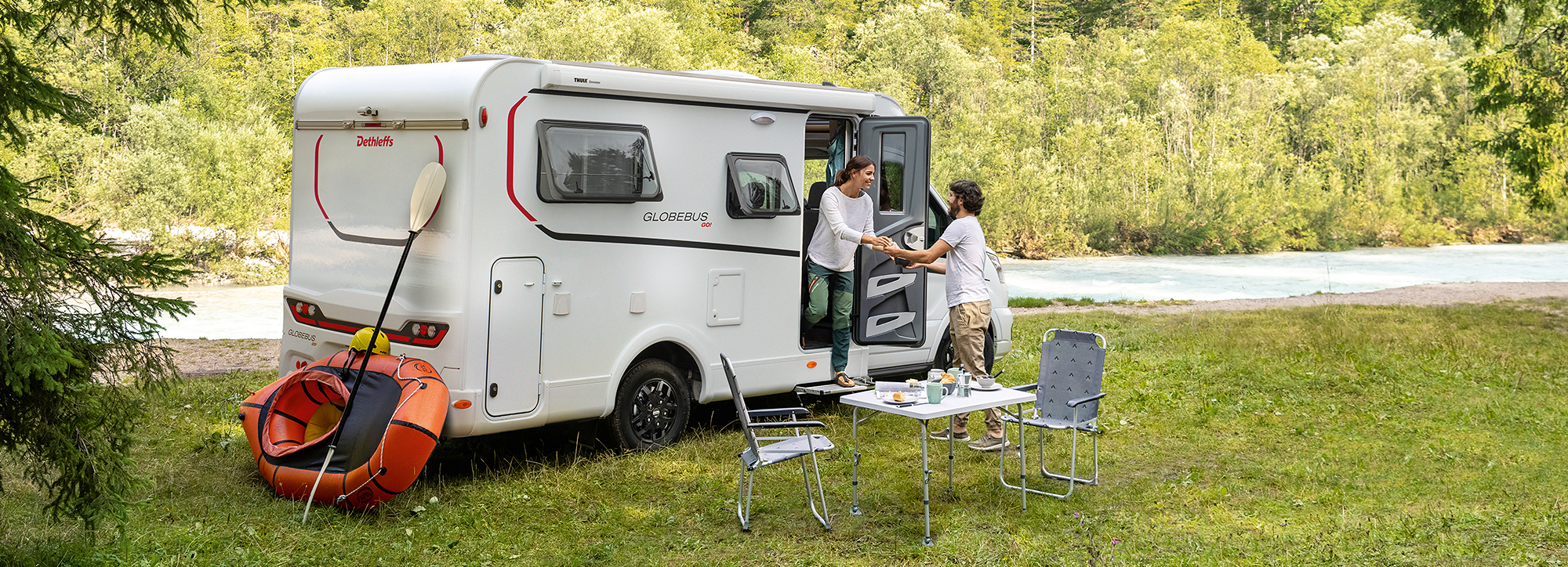 Ein Paar deckt den Frühstückstisch neben einem Wohnmobil.