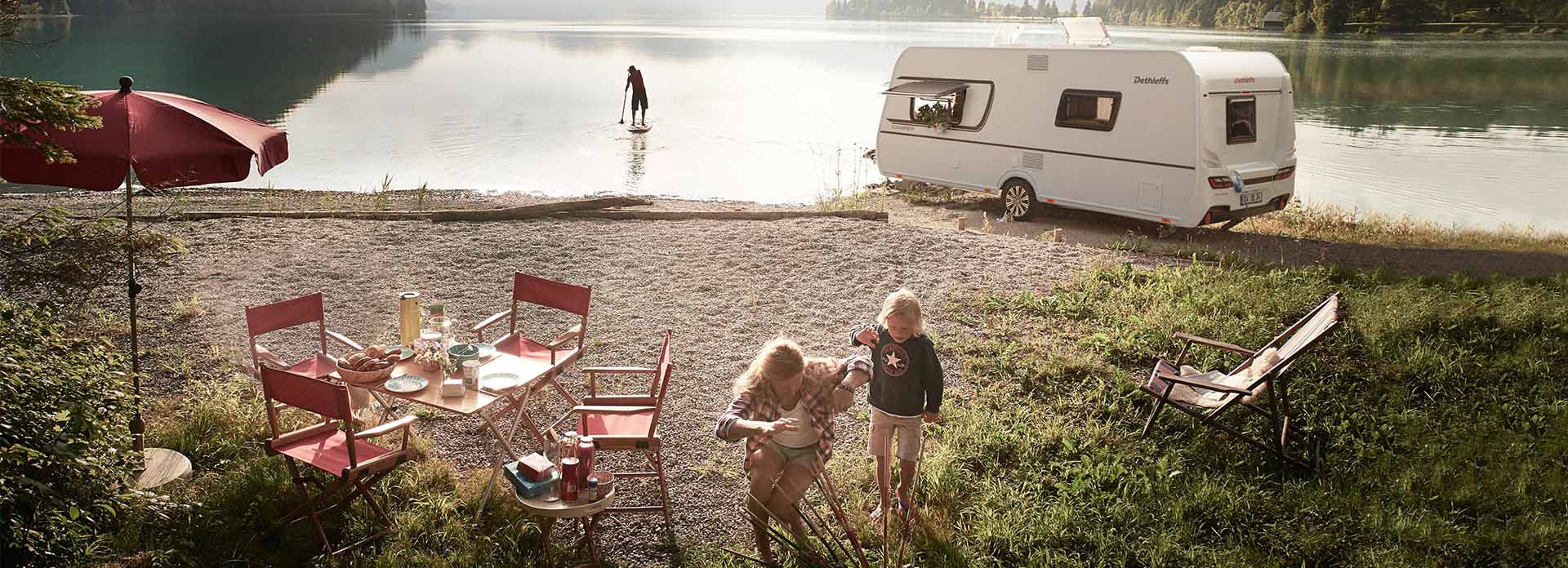 Eine Familie spielt am See neben einem Wohnwagen.