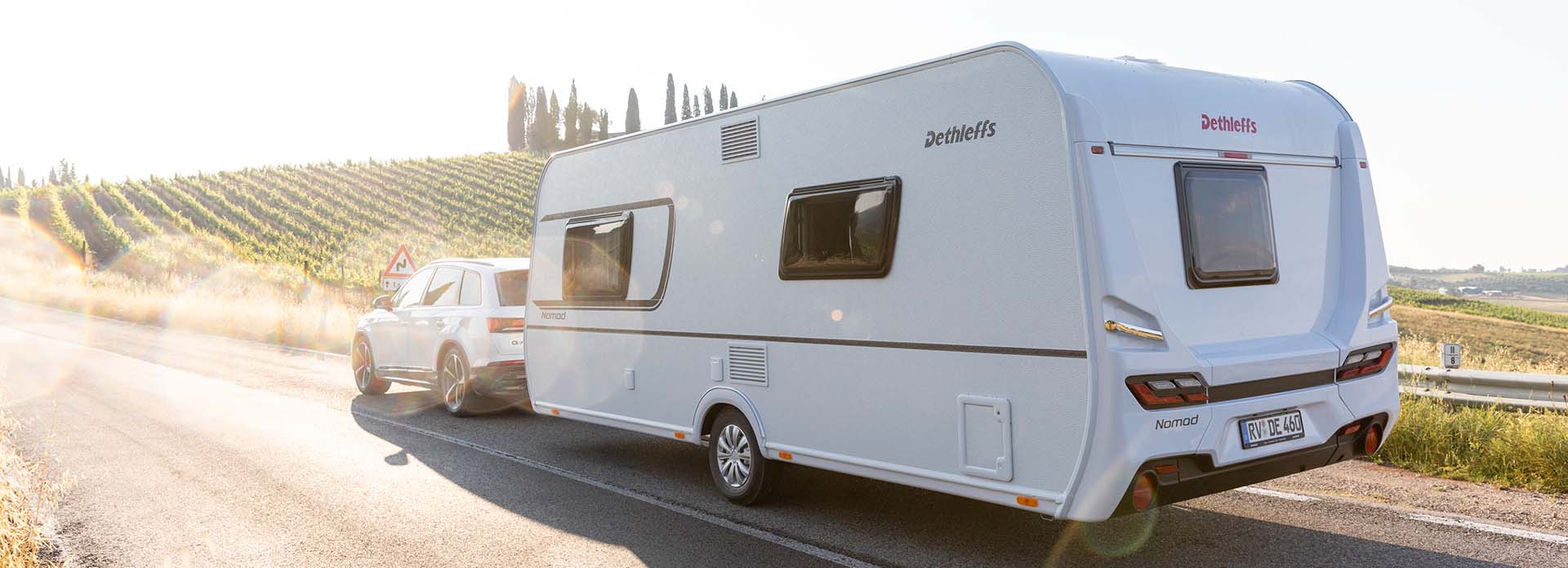 Ein Wohnwagen wird eine Straße im Gegenlicht entlanggezogen.